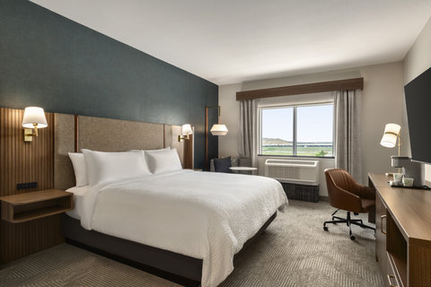 Hotel guest room with a king bed, workspace, and window view.