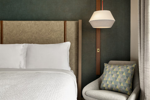 Queen bed with a cozy reading chair and pendant lighting.